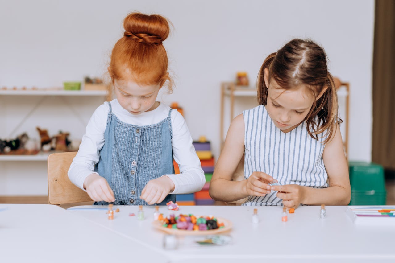 Two young girls actively engaged in a creative project at a classroom table, fostering education and creativity.